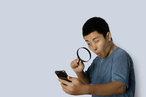 Hombre Joven Mirando Través Lupa Teléfono Inteligente Sobre Fondo Gris —  Fotos de Stock