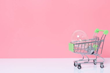 Alışveriş arabasındaki ampul pembe arka planda ve fotokopi alanı var. Fikir kavramı ve ilham.