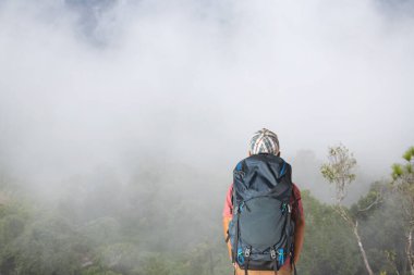 Sırt çantalı genç adam dağda günbatımının tadını çıkarıyor. Vadi manzaralı turist gezgini.