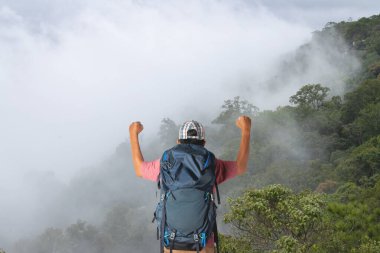 Sırt çantalı genç adam dağda günbatımının tadını çıkarıyor. Vadi manzaralı turist gezgini.