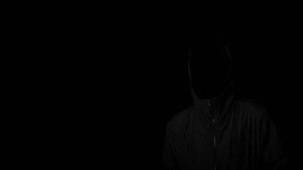 Scary and creepy man hiding in the shadows, with the face and identity hidden with the hood, Dark mysterious man in hoodie on black background. copy space. Concept for fear, mystery, danger, hacker.