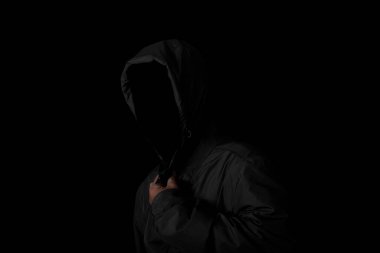 Scary and creepy man hiding in the shadows, with the face and identity hidden with the hood, Dark mysterious man in hoodie on black background. copy space. Concept for fear, mystery, danger, hacker.