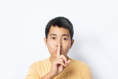Young man making hush gesture and keep conspiracy isolated on white background. Silence and secret concept. copy space
