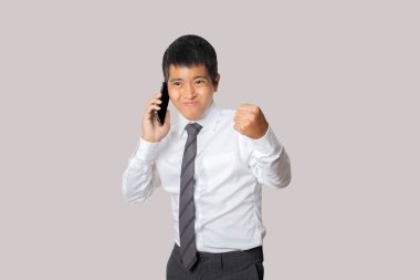 Portrait of businessman talking smartphone with winner gesture and celebrating victory happy. Human emotion face expression concept. Studio shot isolated on gray background. copy space.