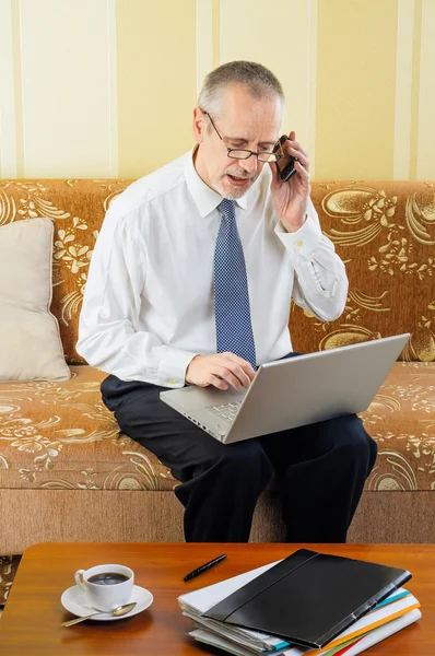 Senior zakenman met computer en mobiele telefoon — Stockfoto