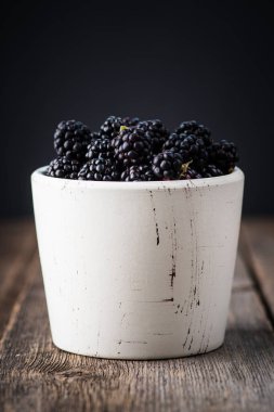 Kırsal ahşap arka planda seramik kasede böğürtlen. Seçici odaklanma. Sığ alan derinliği.