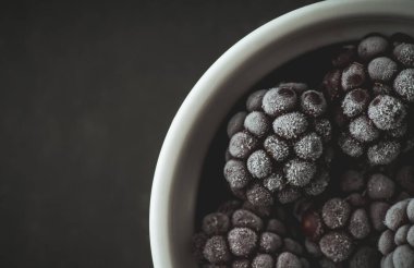 Kırsal ahşap arka planda seramik kasede donmuş böğürtlen. Seçici odaklanma. Sığ alan derinliği.