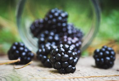 Bahçedeki bir kavanozdan taze böğürtlen dökülüyor. Seçici odaklanma. Küçük alan derinliği.