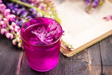 Bir bardak buzlu su ve lupin çiçekli eski bir kitap. Yaz havası. Seçici odaklanma. Sığ alan derinliği.