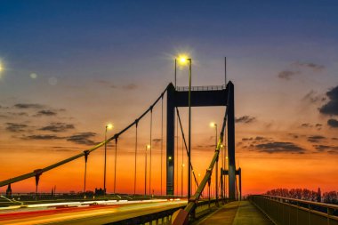 Duisburg Ruhrort 'ta, Ren nehrinin karşısındaki köprüde, alacakaranlıkta, aydınlık patikalarla.