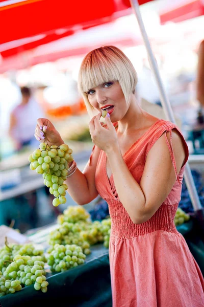 Kvinna provsmakning druvor på marknaden — Stockfoto