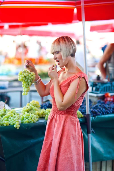 Kvinna provsmakning druvor på marknaden — Stockfoto