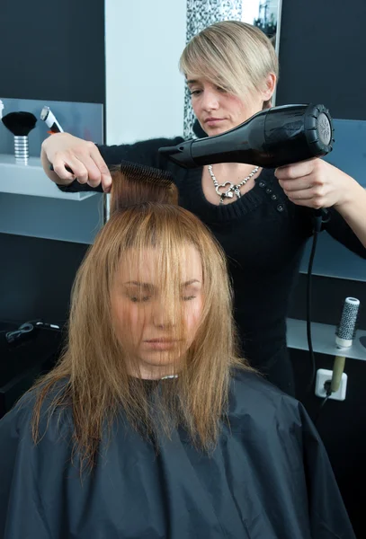 Haarstylistin trocknet Frauenhaare — Stockfoto