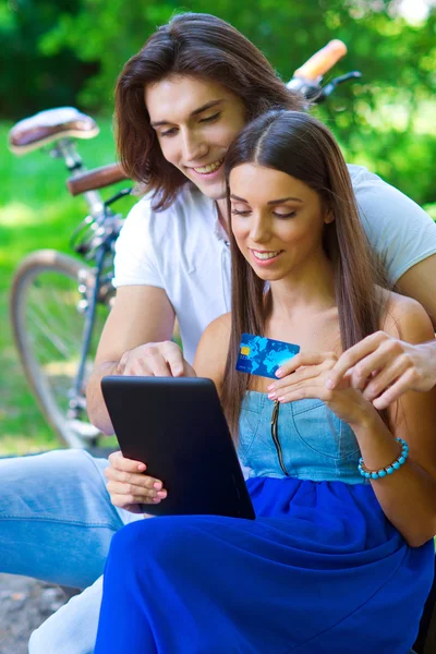 Jovem casal no banco do parque com cartão de crédito e tablet — Fotografia de Stock