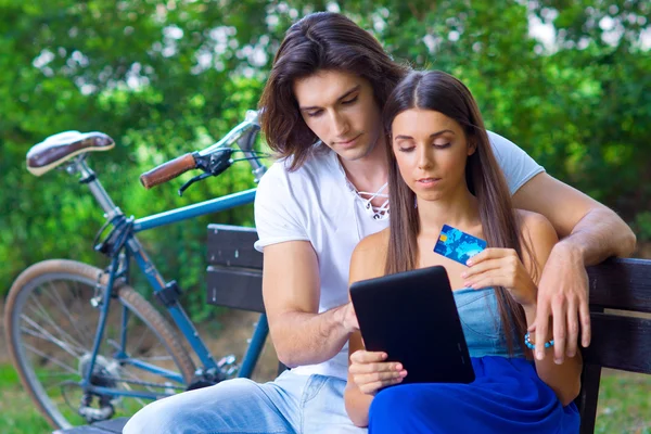 在公园的长凳上与信用卡和平板电脑上的年轻夫妇 — 图库照片