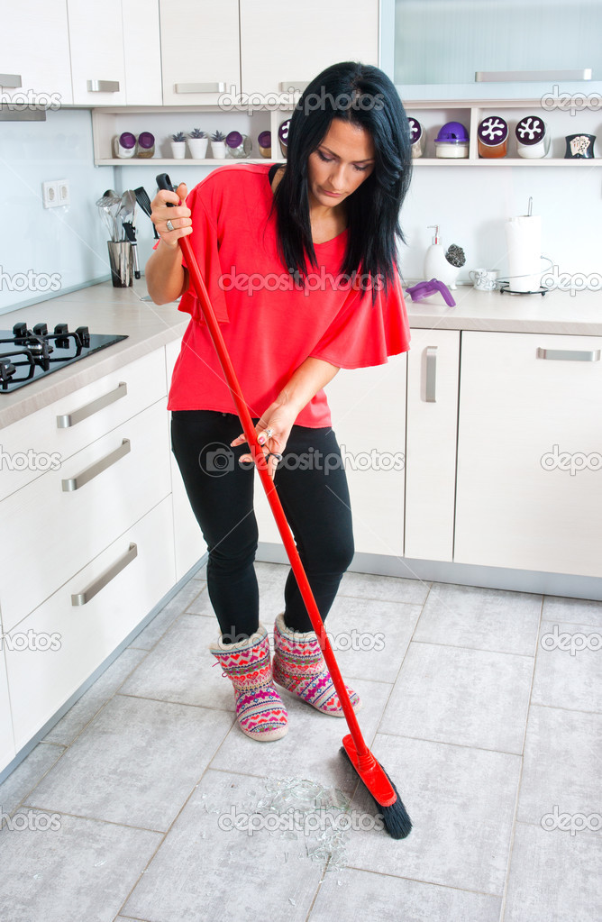 attractive woman cleaning broken glass in kitchen