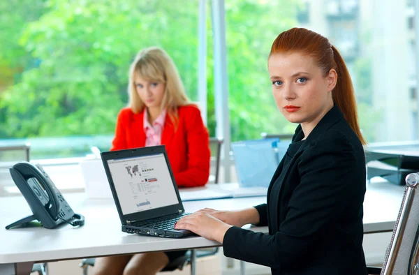 Attractive business woman in office with colleague in background — Stock Photo, Image