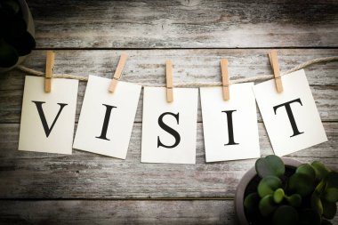 Eski ahşap bir arka planda VISIT sözcüğünü heceleyen basılı kartlar..