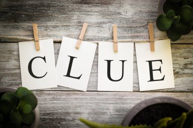 Eski ahşap bir arkaplanda CLUE sözcüğünü heceleyen bir dizi basılı kart.