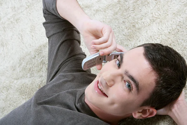 Junge telefoniert mit Handy, während er sich zu Hause auf einen pelzigen Teppich legt. — Stockfoto