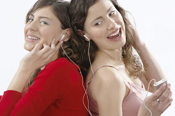 Deux filles dos à dos, écoutant de la musique partager des écouteurs et souriant . — Photo