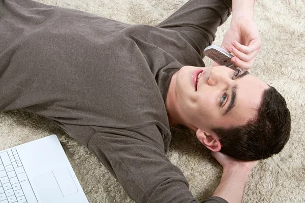 Junge telefoniert mit Handy, während er sich auf pelzigen Teppich legt — Stockfoto