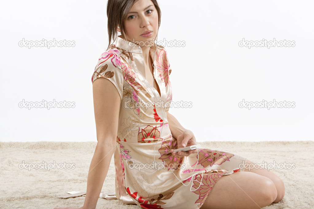 young woman relaxing and sitting on the carpet at home while listening to music with her earphones.