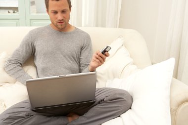 bir dizüstü bilgisayar ve akıllı telefon kullanan genç adam