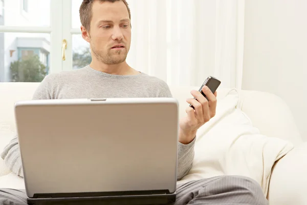 Jovem usando um laptop e um telefone inteligente — Fotografia de Stock