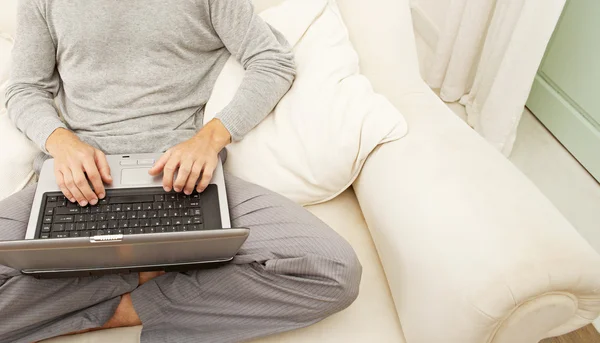 Corpo do homem sentado em um sofá branco e usando um computador portátil . — Fotografia de Stock