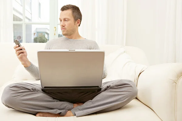 Jovem usando um laptop e um telefone inteligente — Fotografia de Stock