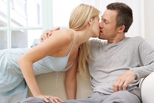 Ungt par kyssas medan på en vit soffa hemma. — Stockfoto