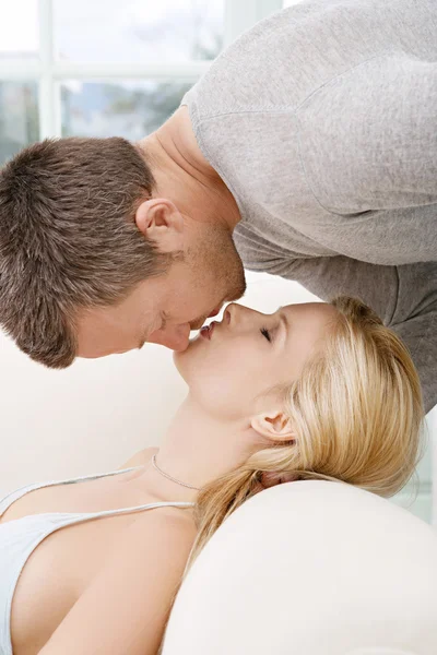 Hombre besar a la mujer mientras descansa en un sofá en casa . —  Fotos de Stock
