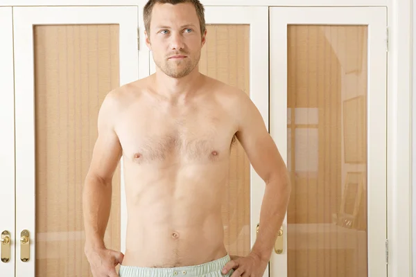 Attractive young man standing by wardrobe doors in a bedroom in underwear. — Stock Photo, Image