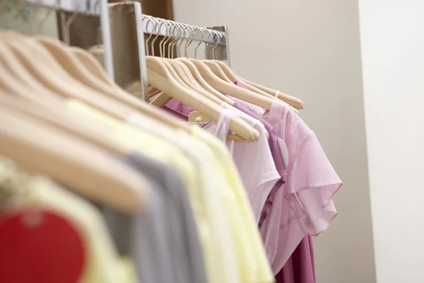 Detalle de la ropa colgada en perchas de madera en una tienda de moda . — Foto de Stock