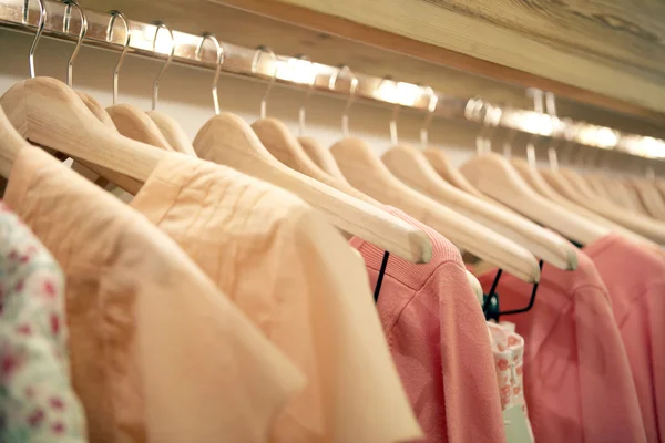 Detalle de ropa rosa colgada en perchas de madera en una tienda de moda . — Foto de Stock
