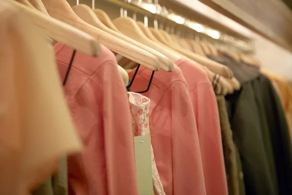 Detalle de la ropa colgada en perchas de madera en una tienda de moda . — Foto de Stock