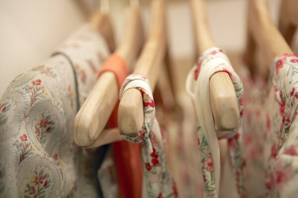 Detail of floral clothes hanging on wooden hangers in a fashion store.