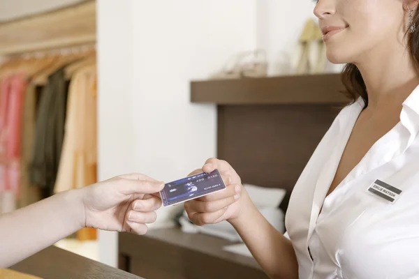 Close up of client's hand handing over credit card to a smiling store attendant. — Stock Photo, Image