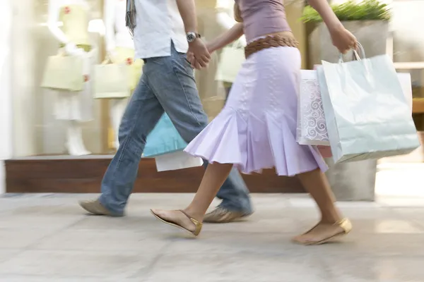 Par gå ner en shoppinggata med kassar, hand i hand. Stockfoto