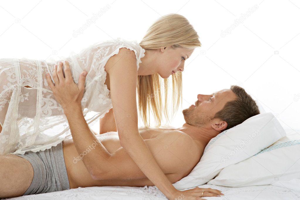 Woman crawling over man in bed, being playful and smiling.