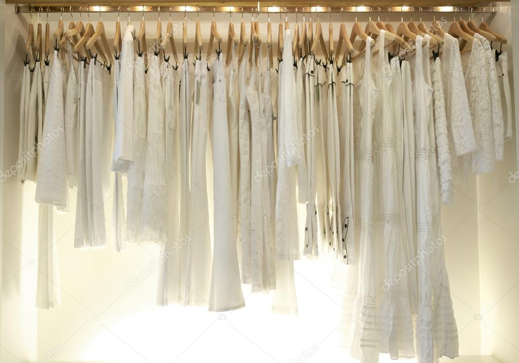 Line of new white clothes hanging on wooden hangers in a fashion store.