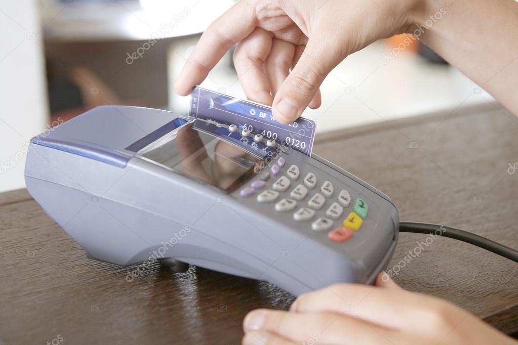 Close up of a store attendant's hand sweeping a credit card in a card reader.