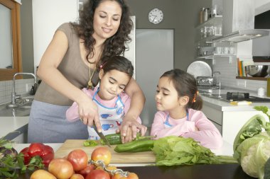 İkiz kızları bir aile ev mutfak ile doğrama sebze genç anne.