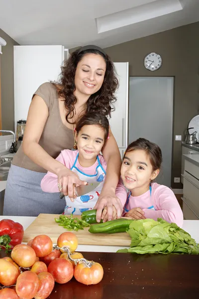 Jovens crianças da família aprendendo a cortar legumes na cozinha com a mãe, sorrindo . — Fotografia de Stock