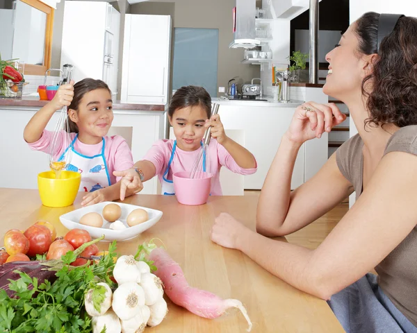 Madre enseñando a las hijas gemelas a batir huevos en la cocina —  Fotos de Stock