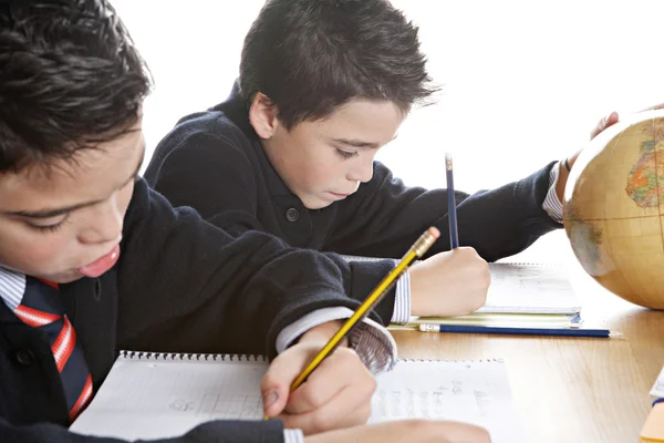 Deux frères jumeaux identiques faisant leurs devoirs de géographie, regardant un globe terrestre assis sur une table en bois à la maison . — Photo