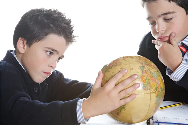 Dois irmãos gêmeos idênticos fazendo sua lição de casa de geografia, olhando para um globo mundial enquanto sentados em uma mesa de madeira em casa . — Fotografia de Stock