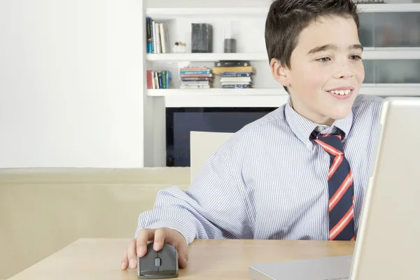 Chłopiec młody szkoły za pomocą myszy i laptop komputer w domu, uśmiechając się. — Zdjęcie stockowe