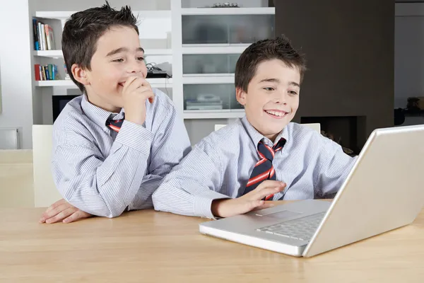 Dos hermanos gemelos idénticos compartiendo una computadora portátil para hacer su tarea —  Fotos de Stock